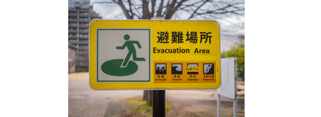 Yellow "Evacuation Area" sign featuring icons for earthquake, tsunami, flood, landslip, and volcanic eruption highlights the importance of Early Warning systems for natural disasters.