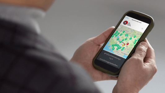 Person holding a mobile phone displaying a map with multiple location markers on the screen.