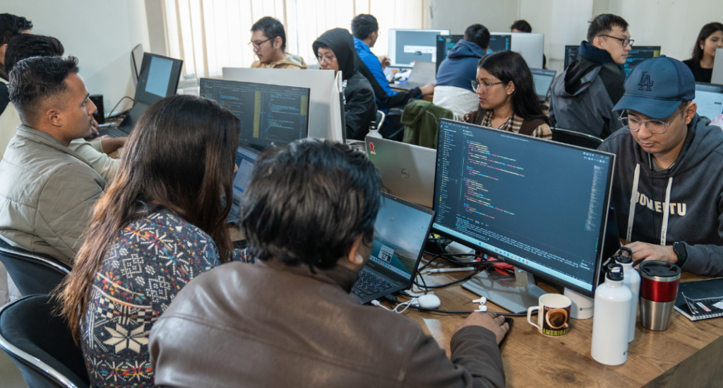 People working on computers with code on screens in a busy, modern office setting focused on innovative climate solutions.