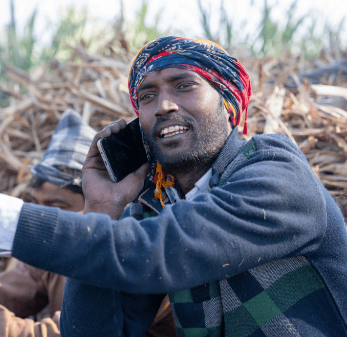 A man in a headscarf smiles while talking on a mobile phone outdoors, with dried plants in the background—perhaps discussing ClimateTech solutions.