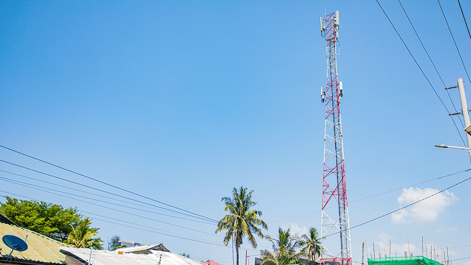 A mobile mast backed by a clear blue sky rises above palm trees and rooftops, symbolising the connectivity advancements driven by initiatives like the GSMA Innovation Fund.
