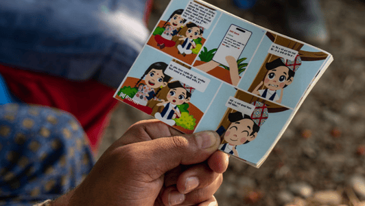 A hand holds a small comic strip featuring animated characters talking in speech bubbles.