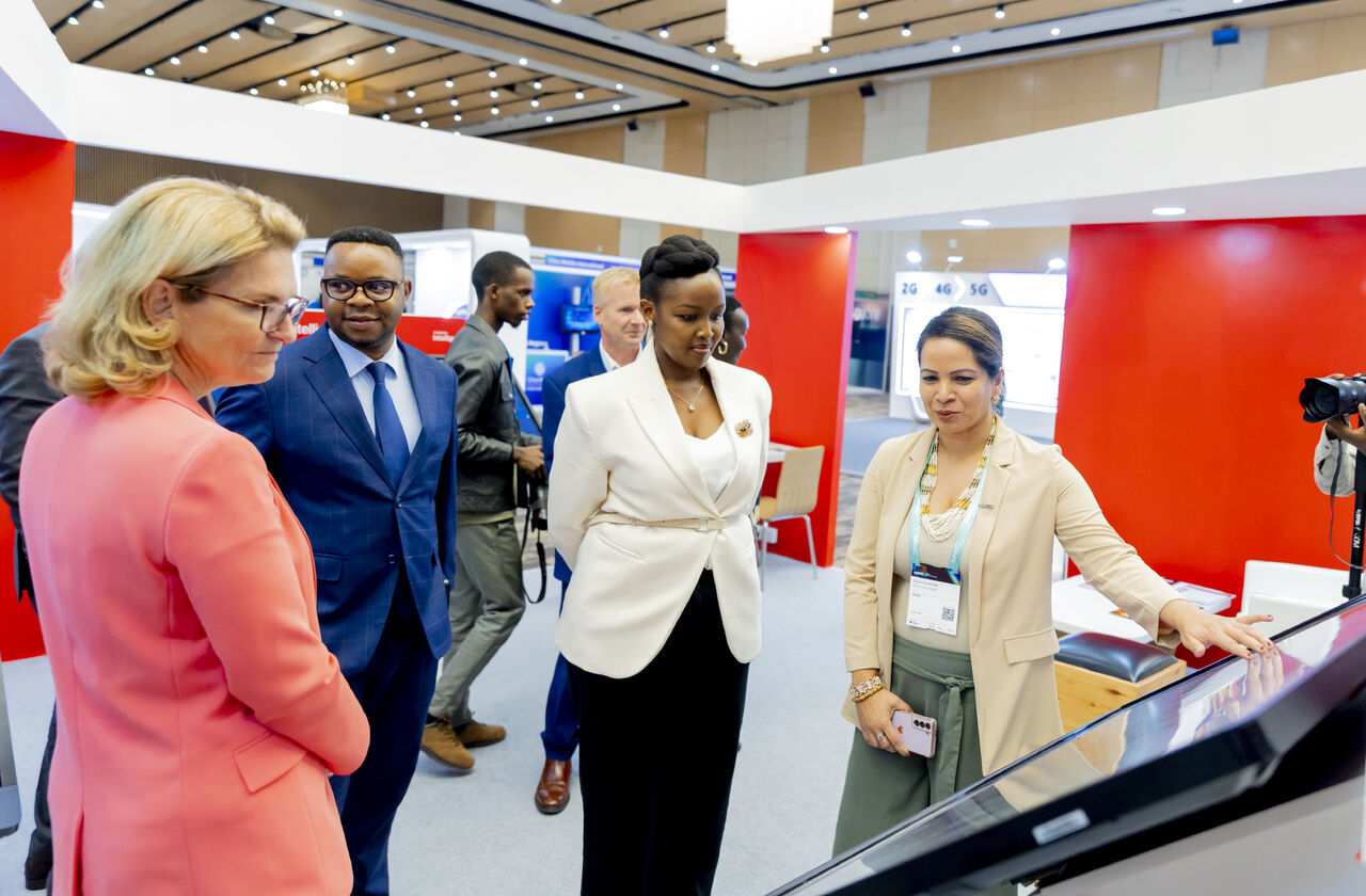 Four professionals stand around a touchscreen display at a business event in a modern, well-lit room.