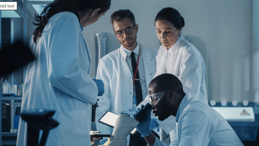 Four scientists in lab coats work together, one with an anticipatory gaze peering into a microscope whilst the others observe closely.