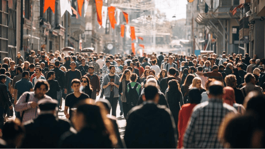 An anticipatory energy fills the crowded city street, with people walking beneath red flags hanging overhead.