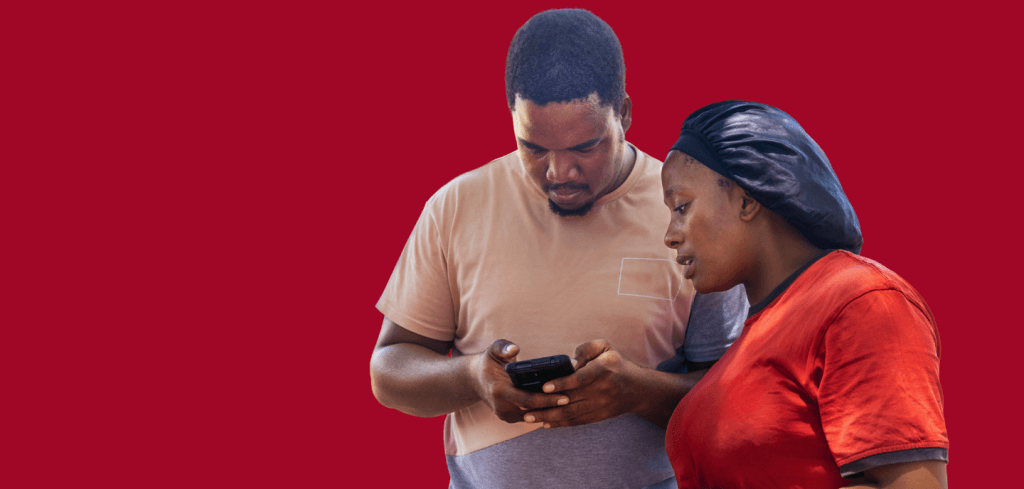 A man and woman look together at a mobile phone, symbolising digital humanitarian assistance, against a solid red background.