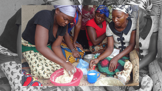 Three women sit together making dough, using bowls and cups, dressed in colourful clothes and headscarves, sharing anticipatory smiles as they prepare for a special meal.