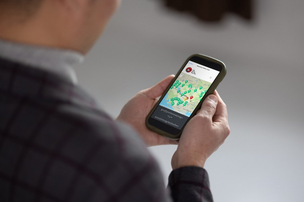 Person holding a mobile phone displaying a map with multiple coloured location pins on the screen.