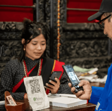 A man scans a QR code at a counter while a woman in traditional attire assists him.