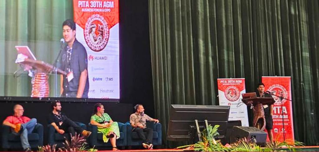 A speaker presents at a lectern on stage while four panellists, discussing early warning strategies, sit beside him at a conference event.