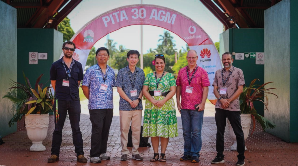 Six people pose together under a PITA 30 AGM event banner outdoors, all wearing name badges and casual clothing.