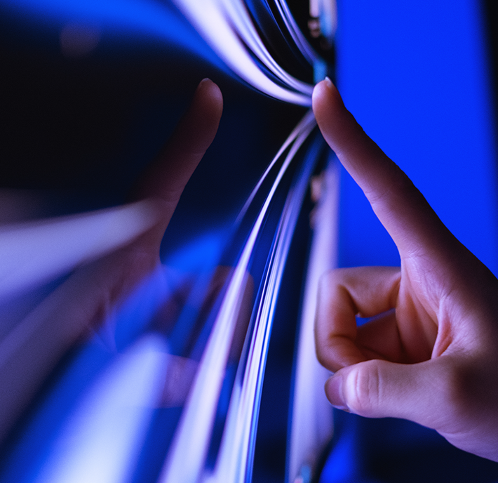 A hand reflected in a curved, blue-tinted mirror surface.