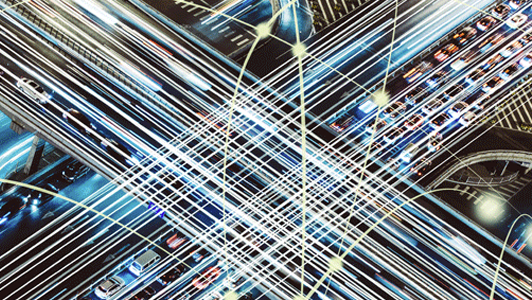 Abstract image of intersecting white light streaks over a blurred background of city traffic and highways at night.