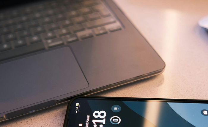 A close-up of a laptop keyboard and an adjacent smartphone emphasizes privacy in the digital age. The laptop focuses on the touchpad, while the smartphone, showing 8:18, sits angled and partially off-screen. Soft lighting casts a warm tone, invoking a sense of calm amidst cybersecurity concerns.