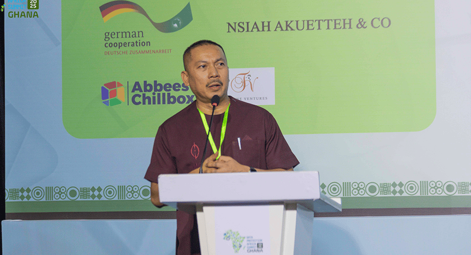 A man stands at a lectern speaking into a microphone, wearing a maroon shirt and blue wristband. Behind him, smart data privacy icons join logos for German Cooperation, Abbees Chillbox, Nsiah Akuetteh & Co on a light backdrop with green and blue accents.