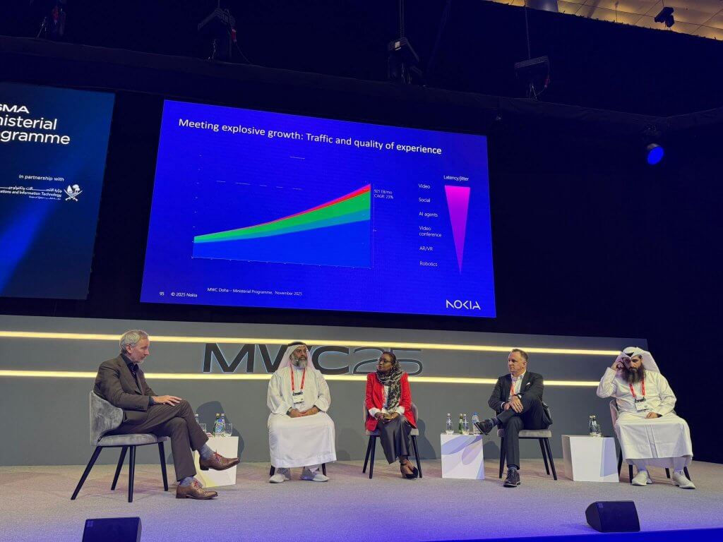 A panel of five people, including three men in traditional Gulf attire, a woman in a red jacket, and a man in a suit, sit on stage. Behind them is a screen displaying a colourful data graph labelled "Nokia." The event backdrop reads "Ministerial Programme.