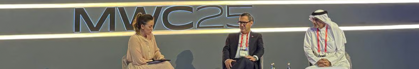 Three people sit on stage in front of a large "MWC25" sign, engaged in a panel discussion as part of the GSMA policy events.