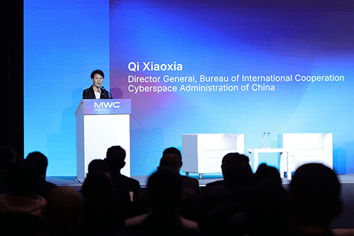 A woman stands at a lectern labeled "MWC," addressing the Policy Leaders Forum Shanghai. The screen behind her displays: "Qi Xiaoxia, Director General, Bureau of International Cooperation, Cyberspace Administration of China." Two empty white chairs are on stage.