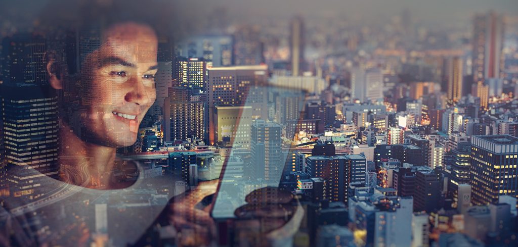 A man smiles while looking at his smartphone, with a cityscape at dusk superimposed over him, blending his image with tall buildings and city lights—symbolizing urban connectivity powered by open-gateway network APIs and next-gen technology.