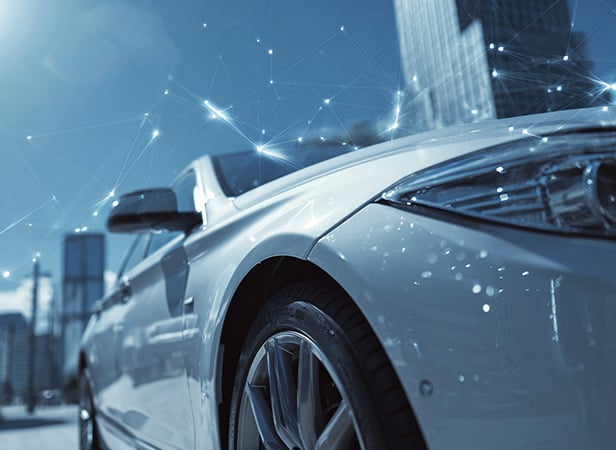 Close-up of a modern silver car in a city with tall glass buildings. Abstract digital network lines highlight automotive APIs, symbolizing smart technology and connectivity in urban environments. The photo has a cool blue tone.