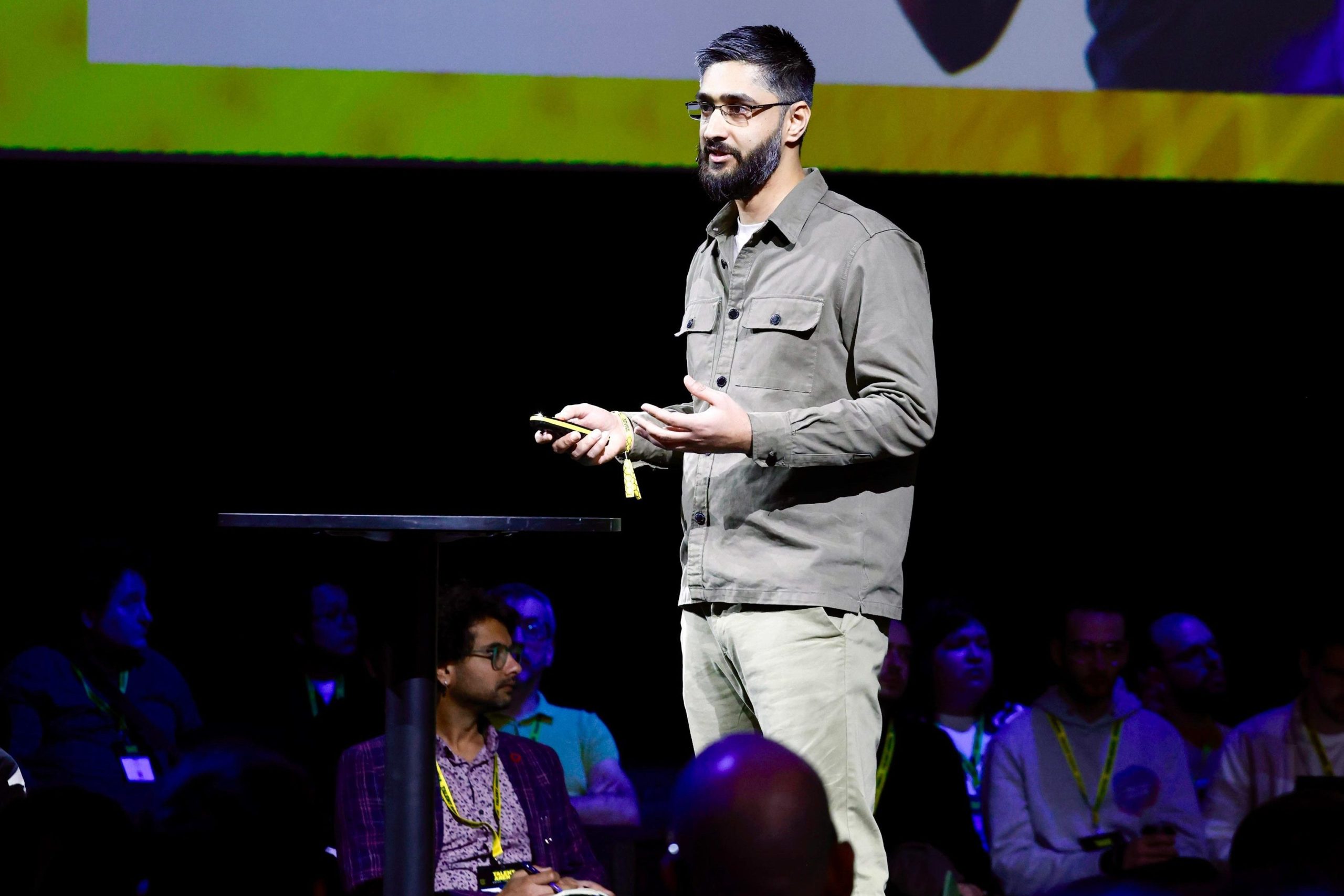 A man presents on stage about developer tools, with a colorful slide and audience in the background.