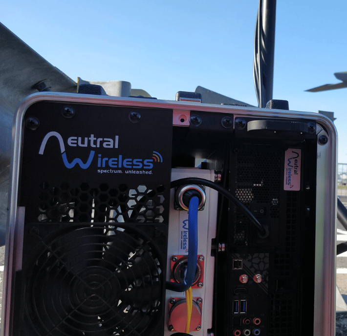 Close-up of Neutral Wireless equipment outdoors, showing cables, ports, and company logo on the device.
