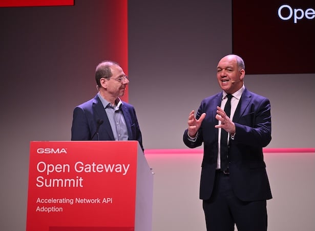 Two men in suits speak onstage at the GSMA Open Gateway Summit, standing behind a red podium.
