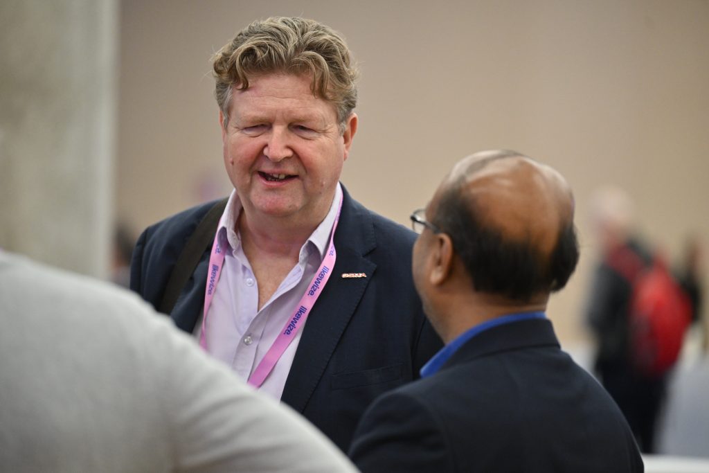 Two men in business attire are having a conversation at an indoor event or conference.