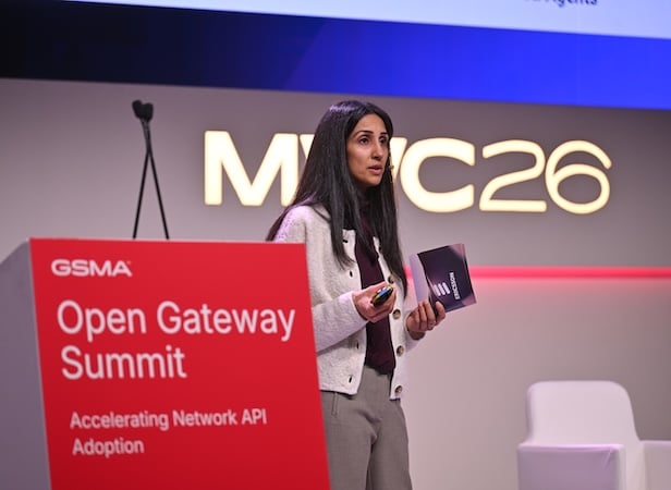 A woman speaks on stage at the Open Gateway Summit during MWC26, holding a notebook and remote, discussing 5G operationalisation and api network monetisation.