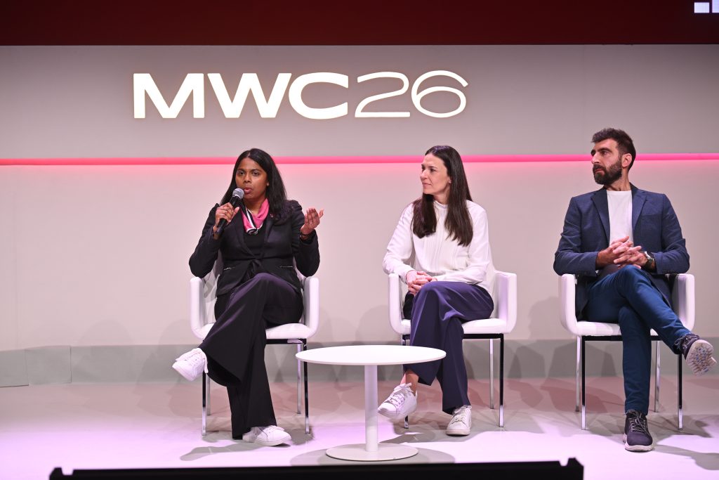 Three people sit on a panel stage at MWC26; the woman on the left speaks into a microphone, discussing 5G operationalisation and api network monetisation strategies.