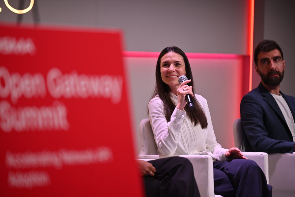 A woman speaks into a microphone at the Open Gateway Summit, seated next to a man, discussing API network monetisation and 5G operationalisation.