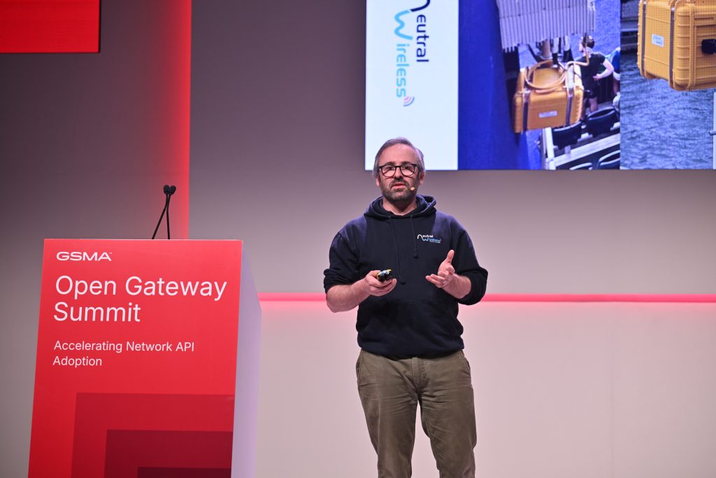 A man speaks on stage at the Open Gateway Summit next to a red podium and large screen, addressing topics like API network monetisation and 5G operationalisation.