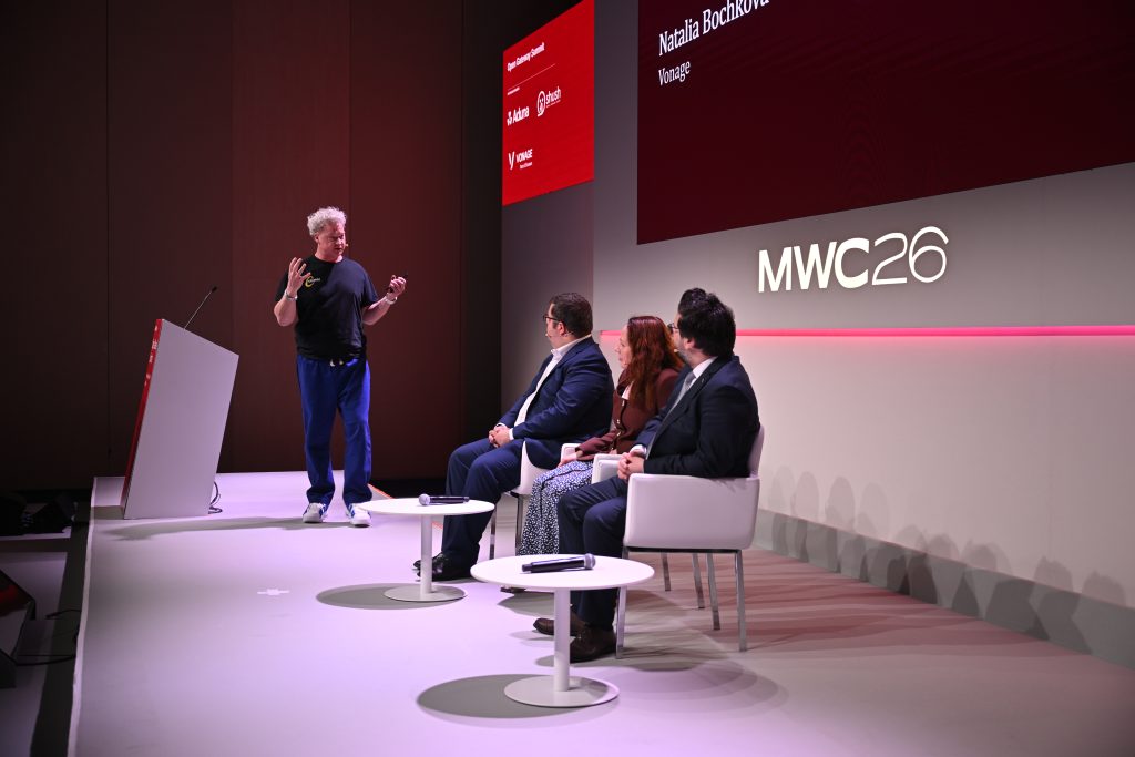 Four people on stage at a conference; one stands speaking about API network monetisation and 5G operationalisation, while three others sit and listen.