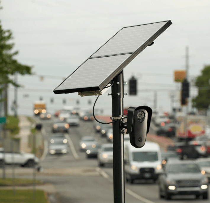 Solar panel and small device, installed on a pole by a busy urban street with cars and traffic lights, highlights the statement of requirements for sustainable city infrastructure.
