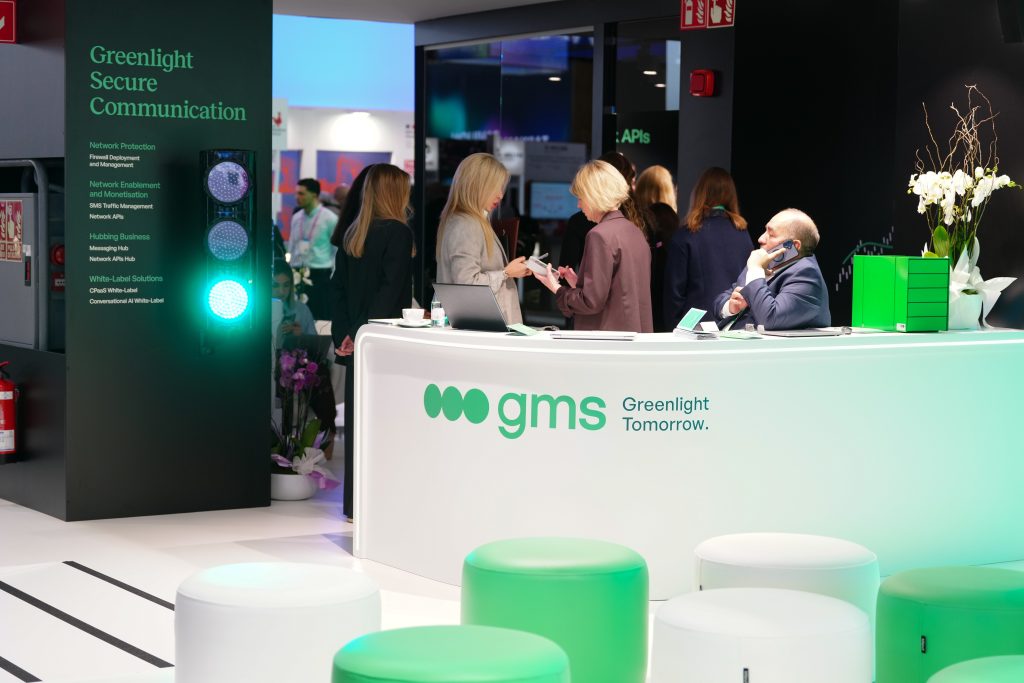 People talking at a white "gms" booth with green lights and signage about secure communication.