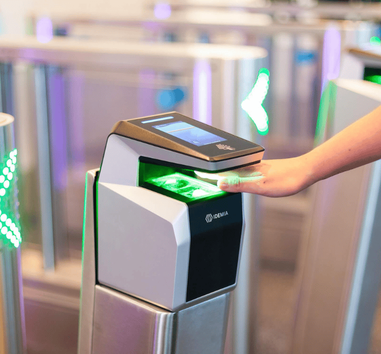 A person scans their hand on a biometric scanner at an automated security gate with green lights.