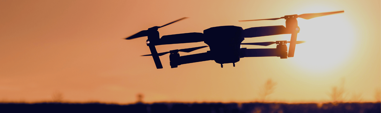 A drone is flying in the air at sunset, silhouetted against an orange sky. Its propellers and structure are clearly visible, while onboard Network APIs enable seamless control as the sun’s warm glow lights up the horizon.