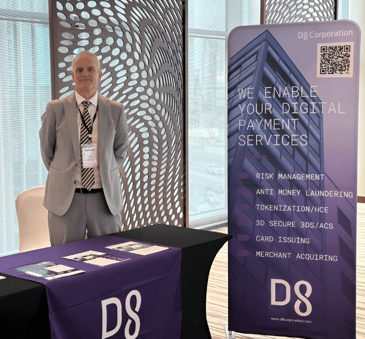 A man in a light grey suit stands at a booth with a purple tablecloth labeled "DS." Behind him is a banner listing digital payment services such as risk management and anti-money laundering, with a tall building graphic and the DS Corporation logo.