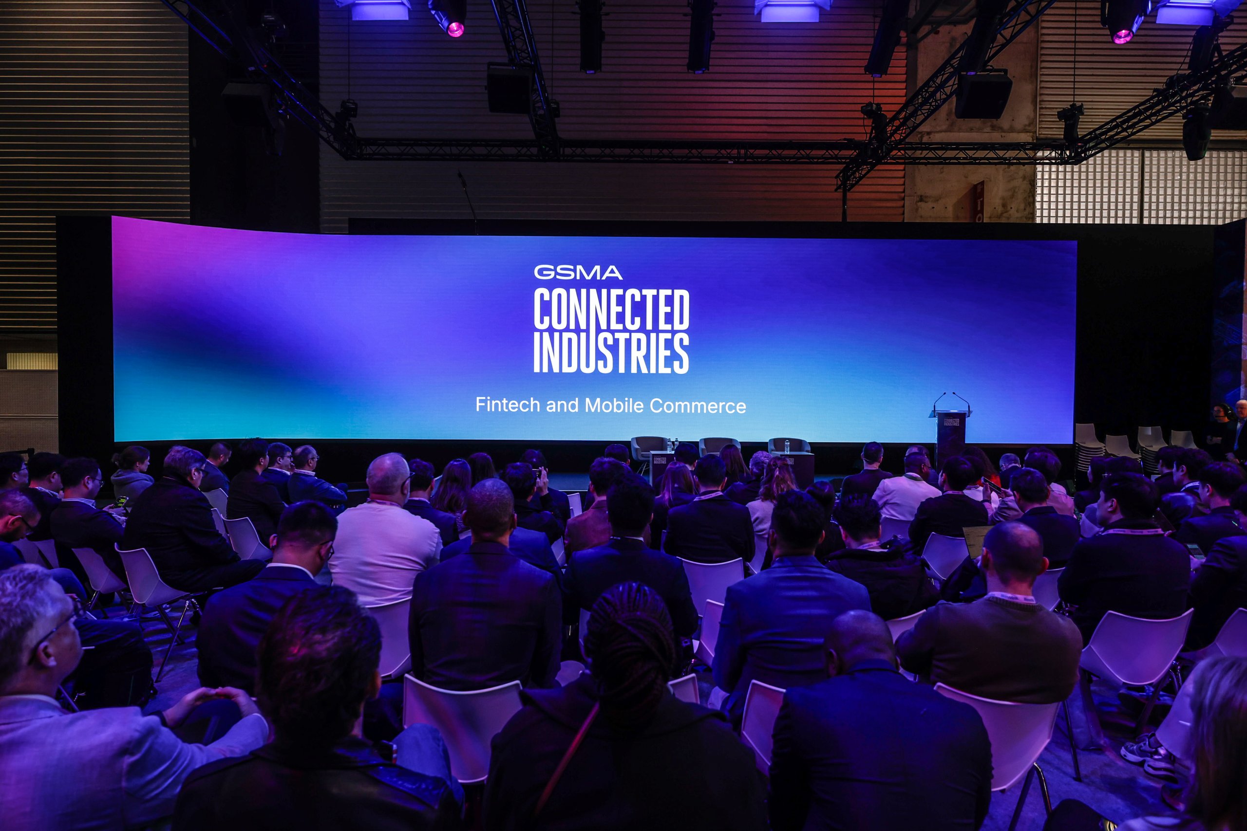 Audience facing a large screen displaying "GSMA Connected Industries: Fintech and Mobile Commerce" at a conference.