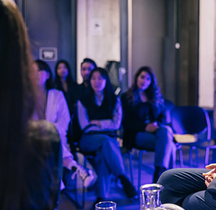 A group of people sit in chairs indoors, listening attentively to someone speaking out of frame about the latest trends in mobile fintech.