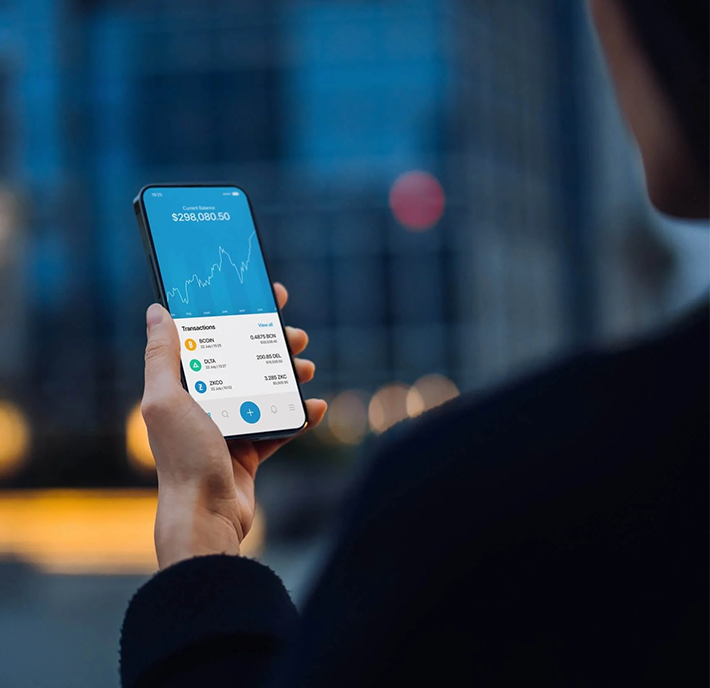 Person holding a smartphone displaying a mobile fintech app with charts and account balances on the screen.