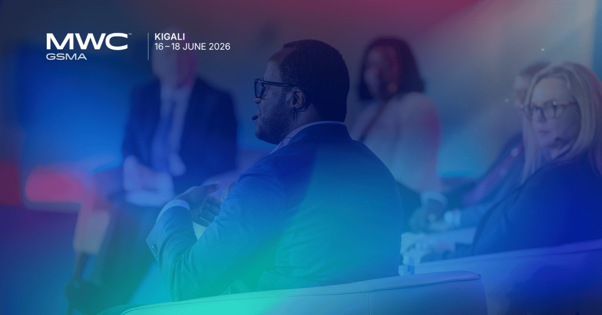 A man with a microphone discusses mobile fintech on a panel at MWC Kigali 2026, while several people listen attentively.