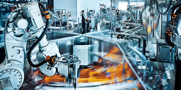 A modern factory floor showcases Connected Manufacturing, with robotic arms assembling products on a conveyor belt. Blurred motion suggests automated, high-speed production as an employee oversees the clean, industrial environment.