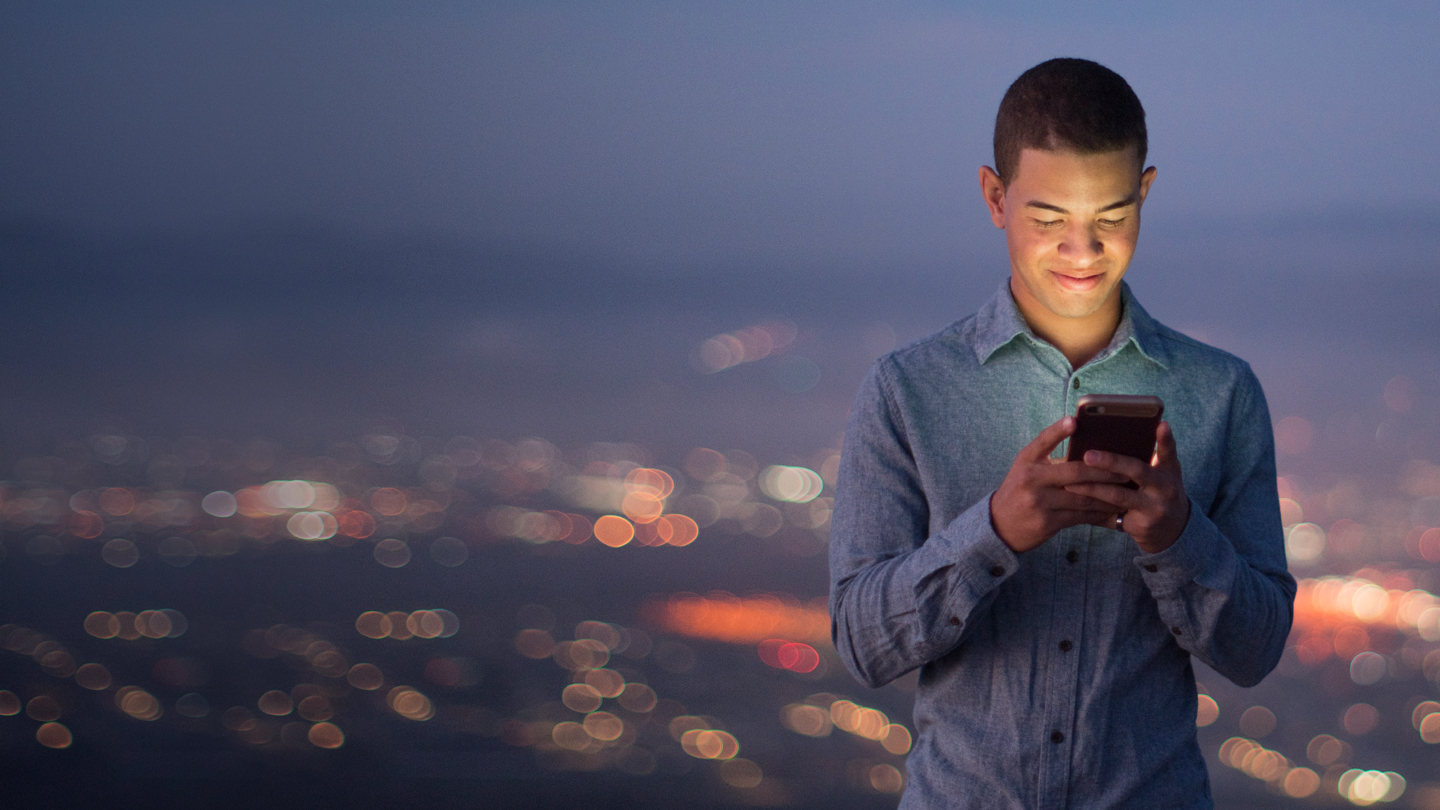 Person looking at mobile phone smiling down on background of cityscape