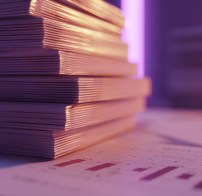 A close-up of a tall stack of documents sits on a desk with soft purple lighting. In the foreground, a sheet with printed bar graphs hints at data analysis, suggesting how AI in mobile could streamline tasks in a modern business setting.