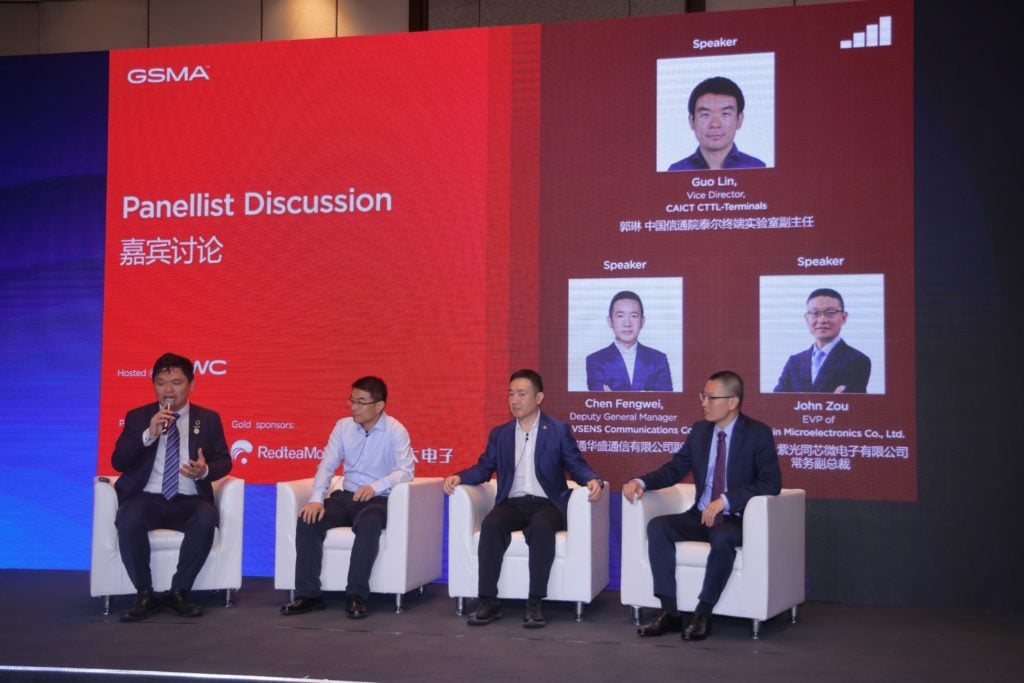 Four men in suits sit on a stage participating in a panel discussion. Behind them, a red screen displays the text "Panellist Discussion" with their names and titles alongside their photos. The event is organized by GSMA, with various logos and text in English and Chinese.