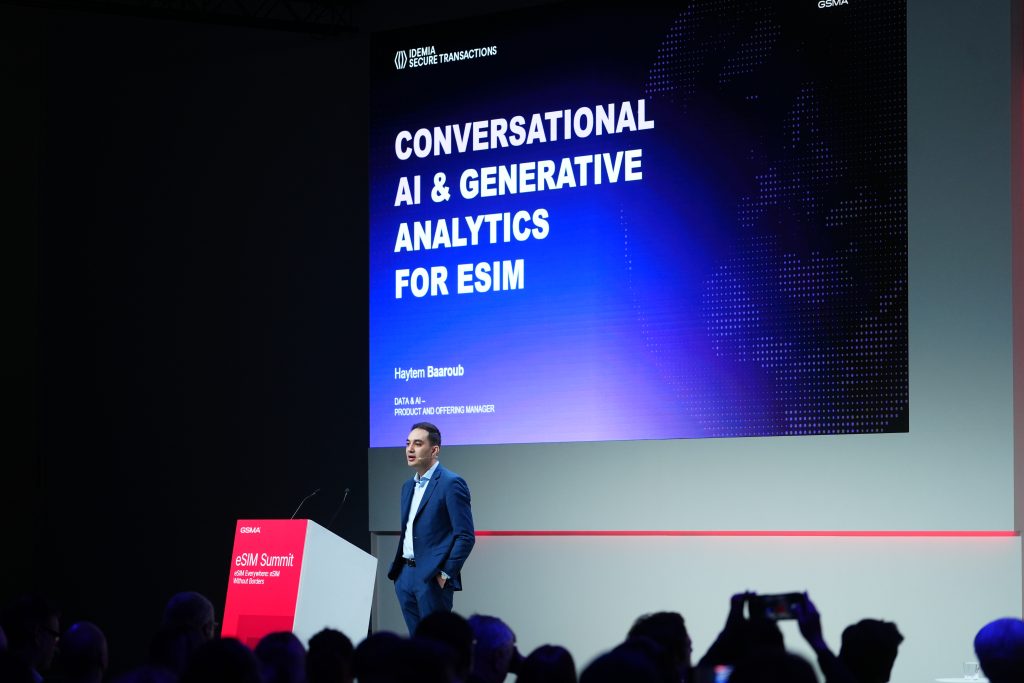 A speaker stands on stage beside a screen displaying "Conversational AI & Generative Analytics for eSIM".