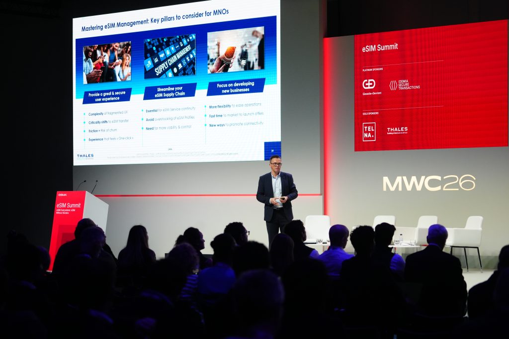 A speaker presents at a tech summit with slides and audience in a modern conference room.