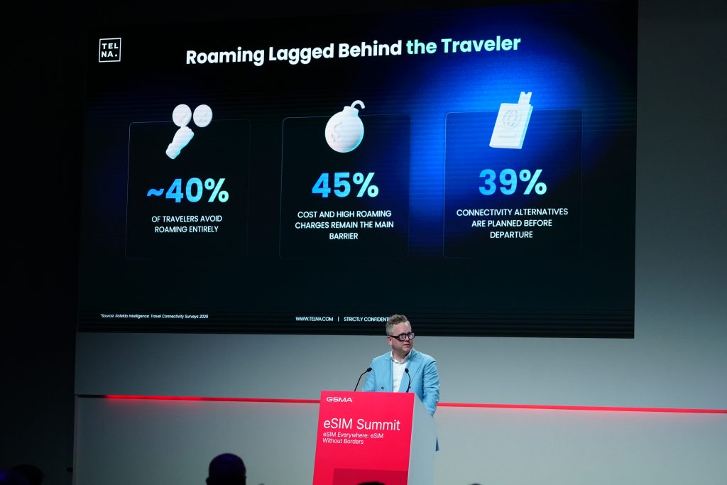 Man presenting at eSIM Summit in front of a screen showing roaming statistics for travellers.