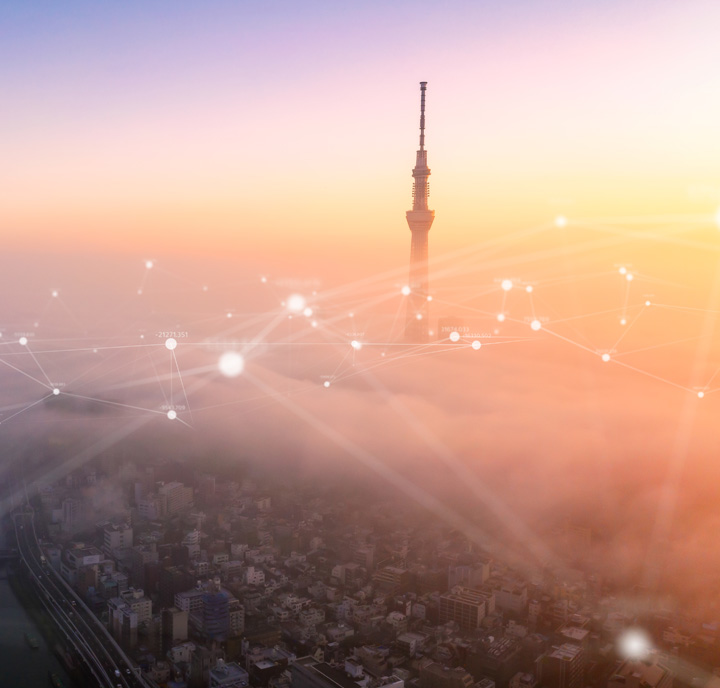 A city skyline at sunrise with a tall tower emerging through fog. Digital lines and glowing nodes overlay the scene, creating a network-like effect in the sky. The warm colors of the sunrise add a soft glow to the cityscape.